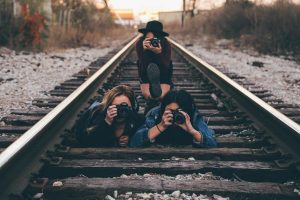 3 women photographers taking pictures while sitting on a railroad track. 