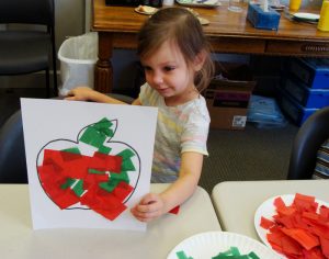 Little girl showing her tissue paper apple craft.