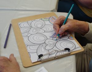 Adult woman's hand coloring a heart printed sheet with a colored pencil.