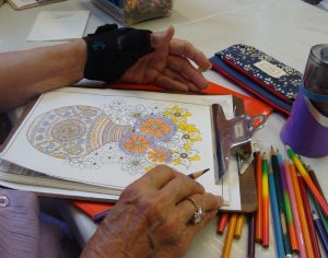 Adult woman's hands coloring a flower coloring sheet with a colored pencil.