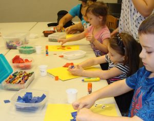Children glueing colored tissue on paper.