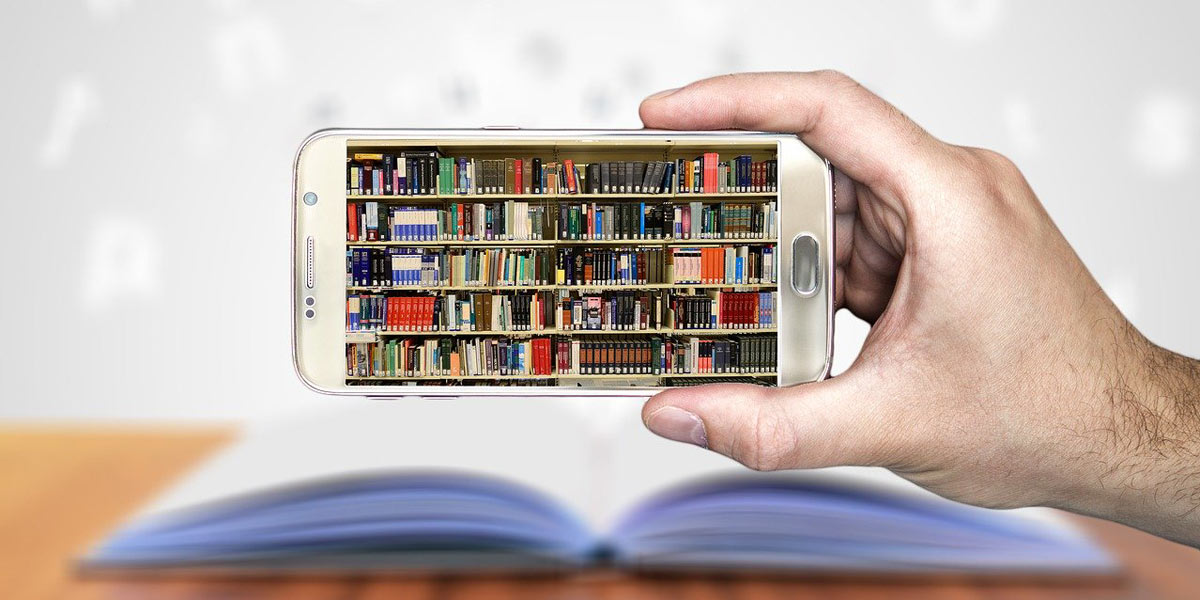 Hand holding a cell phone displaying a picture of library shelves with an open book in the background.